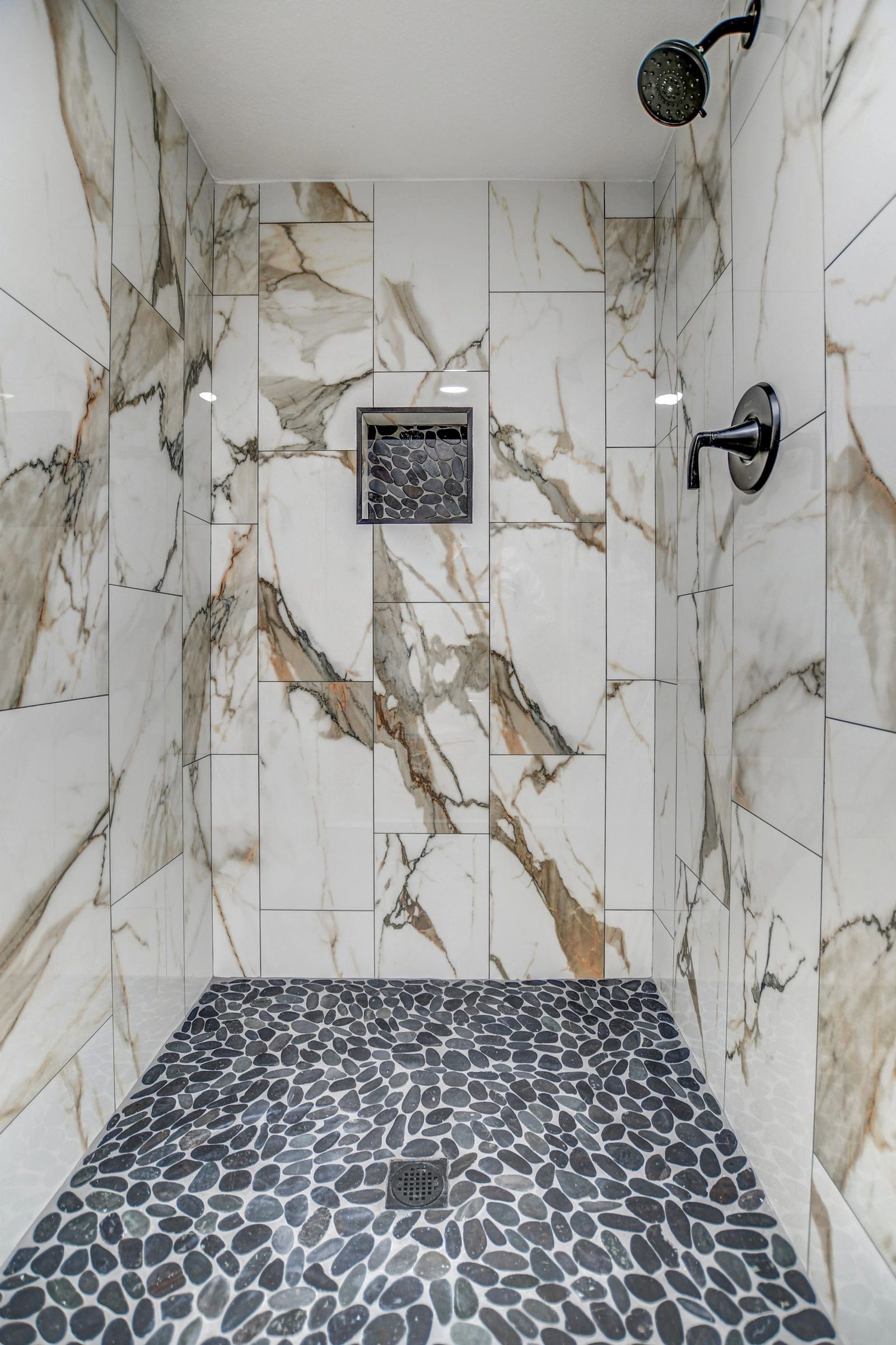 Finished marble tile shower with pebble floor